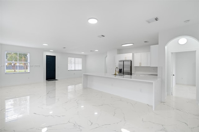 kitchen with stainless steel fridge with ice dispenser, white cabinetry, decorative backsplash, a kitchen island with sink, and sink