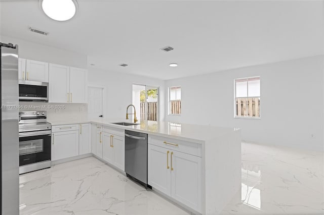 kitchen with kitchen peninsula, appliances with stainless steel finishes, sink, and white cabinetry