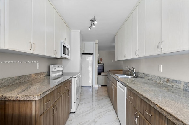 kitchen with sink, white appliances, light stone countertops, track lighting, and white cabinets