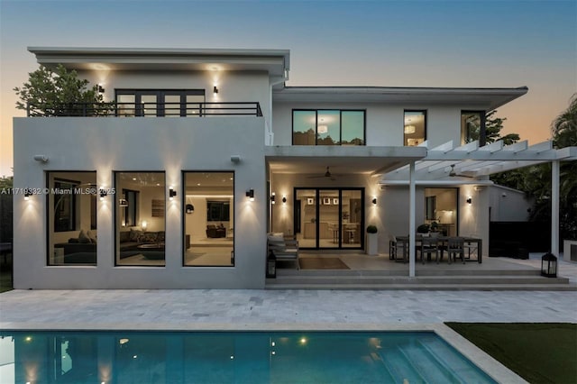 back house at dusk with ceiling fan, a pergola, a balcony, and a patio