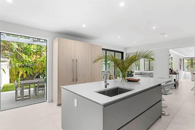 kitchen featuring light tile patterned floors, light brown cabinets, a kitchen island with sink, a kitchen breakfast bar, and sink