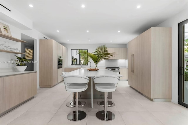 kitchen featuring a breakfast bar area, light brown cabinets, oven, a kitchen island, and sink