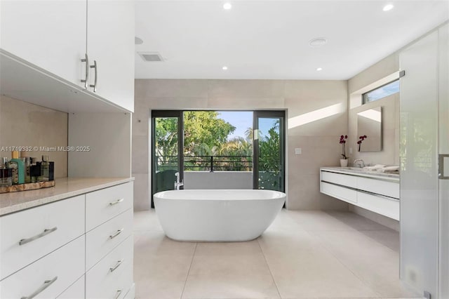 bathroom featuring tile patterned flooring, tile walls, a tub to relax in, and vanity