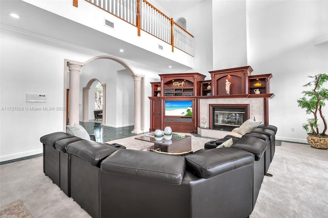 living room featuring a premium fireplace, a high ceiling, ornamental molding, and ornate columns