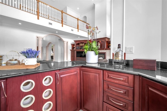 kitchen with a towering ceiling, dark stone counters, crown molding, and decorative columns