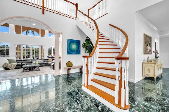 stairs with a towering ceiling, crown molding, and ornate columns