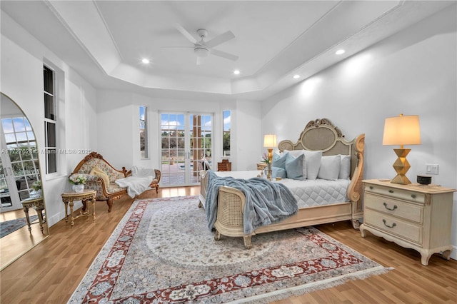 bedroom featuring light wood-type flooring, ceiling fan, access to exterior, and a tray ceiling