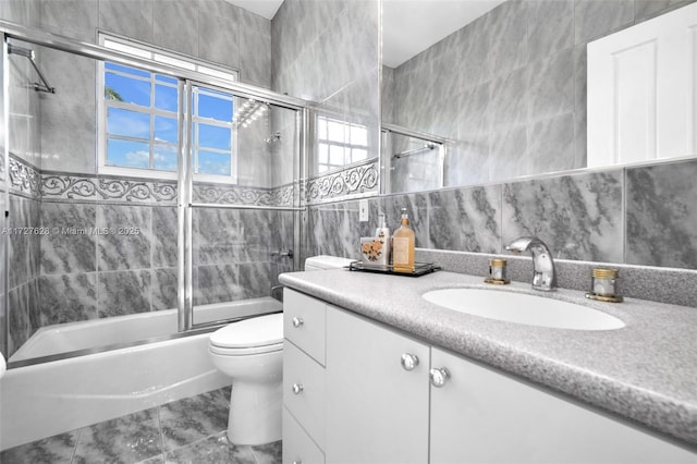 full bathroom featuring tile patterned flooring, vanity, tile walls, toilet, and combined bath / shower with glass door