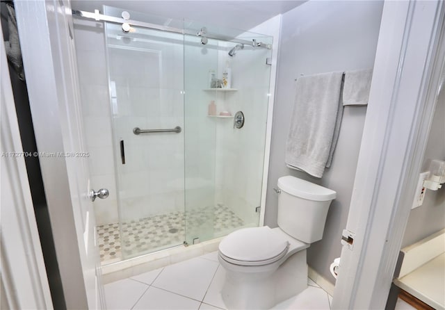 bathroom featuring toilet, tile patterned flooring, and a shower with shower door