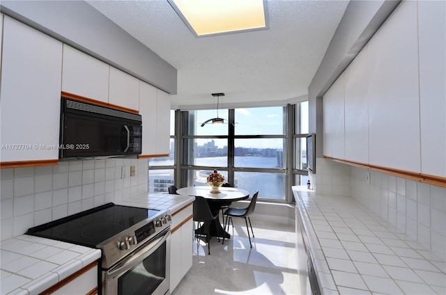 kitchen with stainless steel range with electric cooktop, white cabinetry, decorative backsplash, tile countertops, and a water view