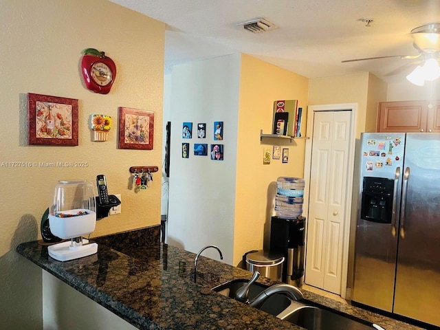 kitchen with stainless steel refrigerator with ice dispenser, sink, kitchen peninsula, and dark stone countertops