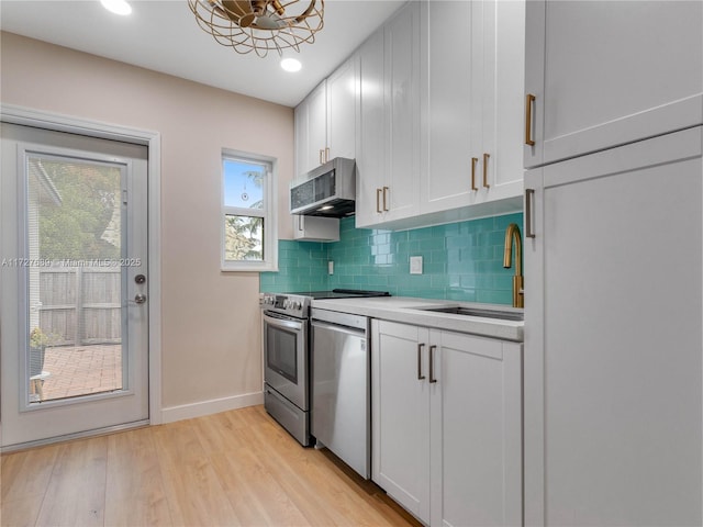 kitchen with sink, white cabinetry, appliances with stainless steel finishes, light hardwood / wood-style floors, and decorative backsplash