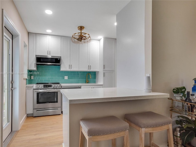 kitchen with a breakfast bar, white cabinetry, decorative backsplash, kitchen peninsula, and stainless steel appliances