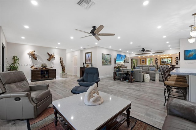 living room with ceiling fan with notable chandelier and light wood-type flooring