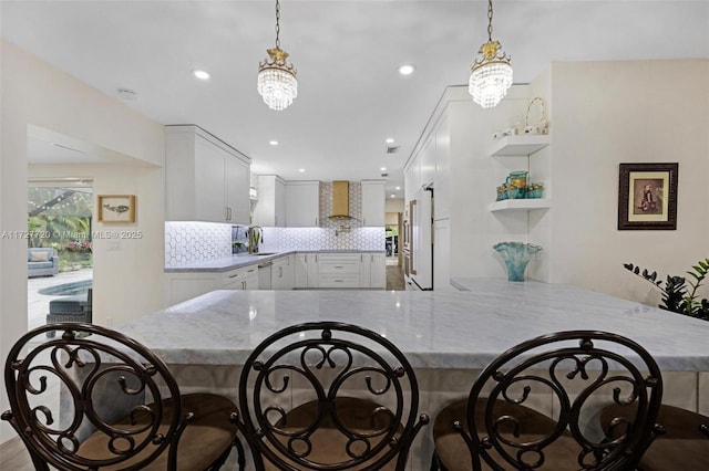 kitchen with kitchen peninsula, pendant lighting, white cabinets, and wall chimney exhaust hood