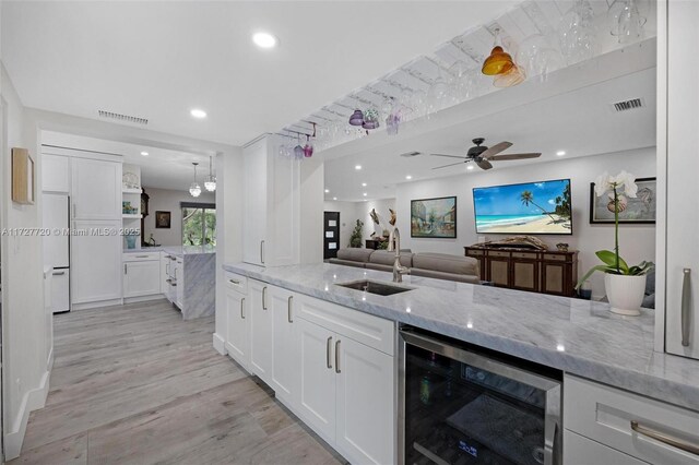 kitchen featuring sink, white cabinetry, light stone counters, beverage cooler, and light hardwood / wood-style floors