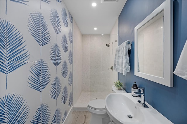 bathroom featuring sink, wood-type flooring, toilet, and tiled shower