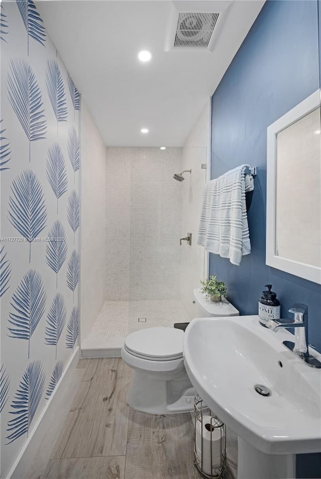 bathroom featuring hardwood / wood-style floors, sink, toilet, and tiled shower