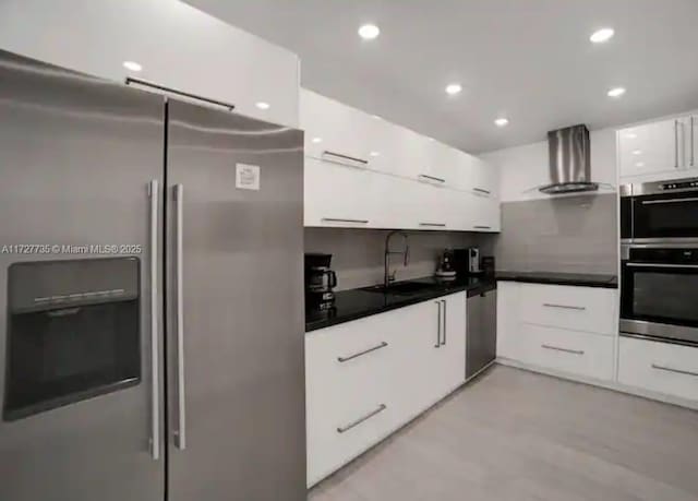 kitchen with stainless steel appliances, sink, white cabinetry, and wall chimney range hood