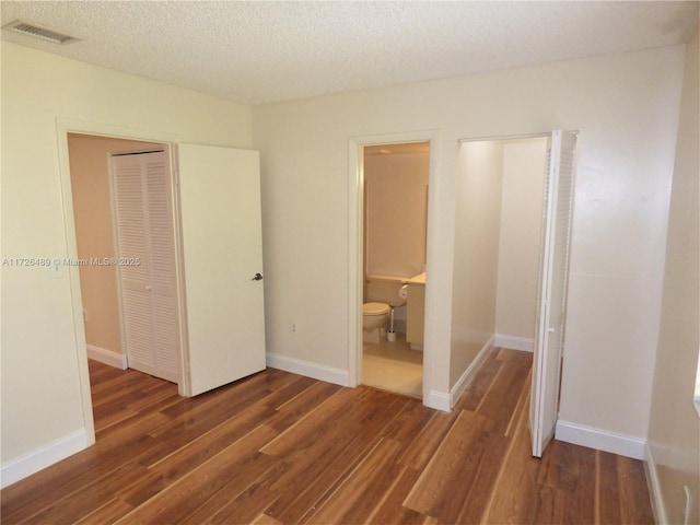 unfurnished bedroom featuring a textured ceiling, a closet, dark hardwood / wood-style flooring, and connected bathroom