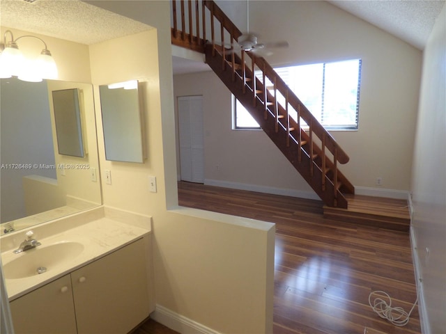 bathroom with ceiling fan, vanity, lofted ceiling, hardwood / wood-style flooring, and a textured ceiling