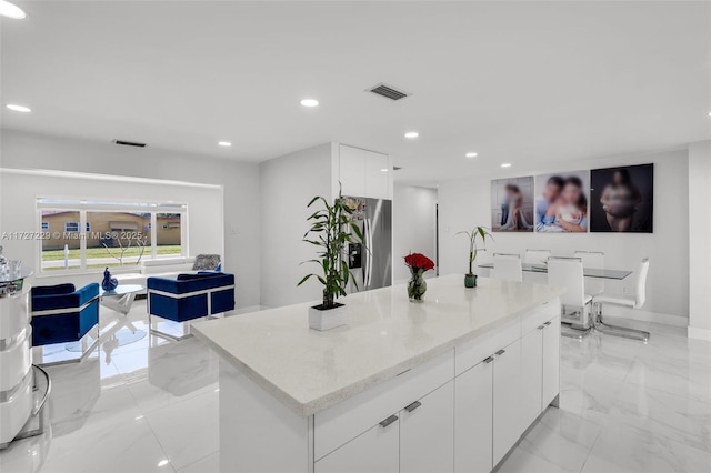 kitchen featuring stainless steel refrigerator with ice dispenser, light stone countertops, white cabinets, and a kitchen island