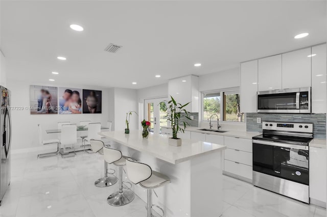 kitchen with white cabinets, a kitchen island, stainless steel appliances, sink, and a breakfast bar area