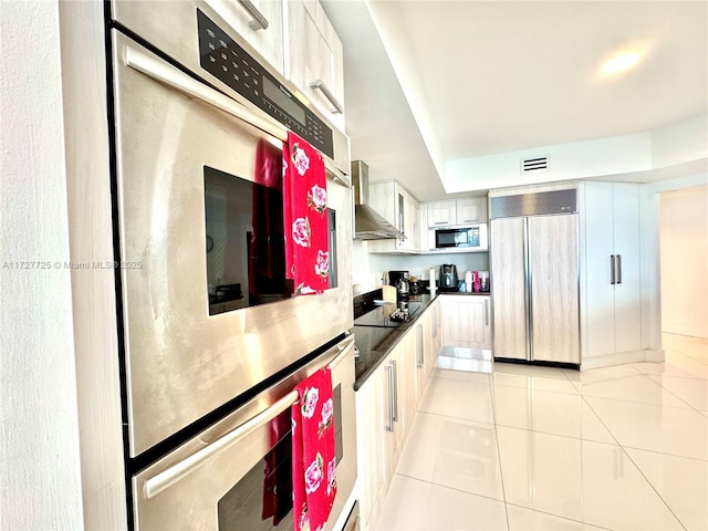 kitchen featuring light tile patterned flooring, built in appliances, white cabinets, and wall chimney exhaust hood