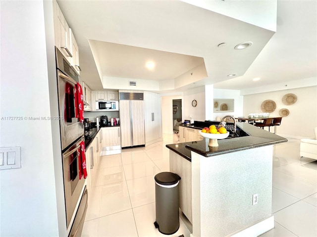 kitchen featuring stainless steel appliances, a tray ceiling, a kitchen island, and light tile patterned floors