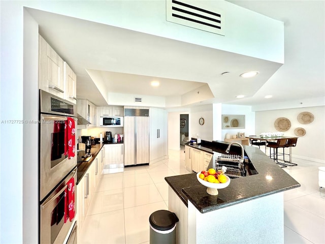 kitchen with sink, white cabinetry, built in appliances, a tray ceiling, and a kitchen island