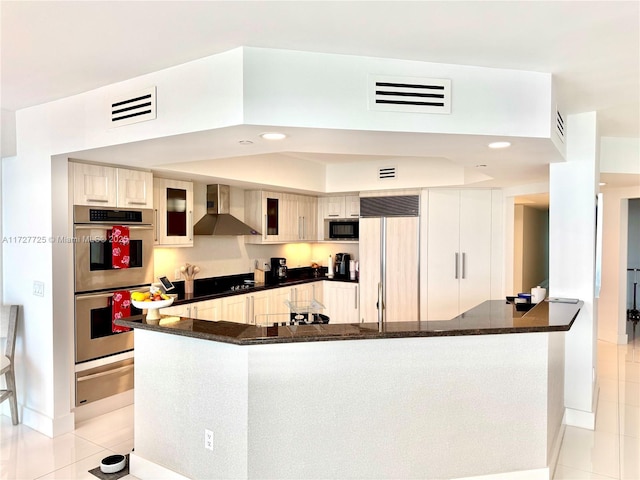 kitchen with black appliances, kitchen peninsula, light tile patterned floors, and wall chimney range hood