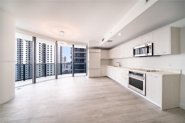 kitchen featuring decorative light fixtures, sink, white cabinetry, stainless steel appliances, and a wall of windows