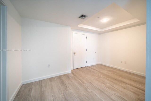 empty room with a tray ceiling and light hardwood / wood-style floors