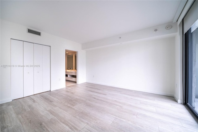 unfurnished bedroom featuring light hardwood / wood-style floors, ensuite bathroom, and a closet