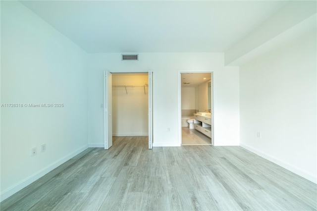 unfurnished bedroom featuring a spacious closet, a closet, light hardwood / wood-style floors, and connected bathroom