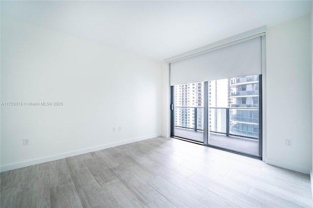 empty room featuring a wall of windows and light hardwood / wood-style flooring