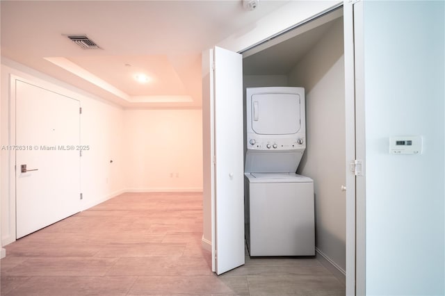 clothes washing area with stacked washing maching and dryer and light hardwood / wood-style flooring