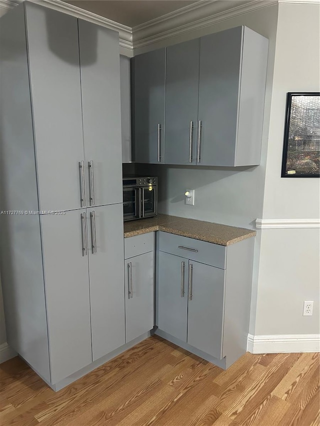 kitchen featuring gray cabinetry, crown molding, and light wood-type flooring