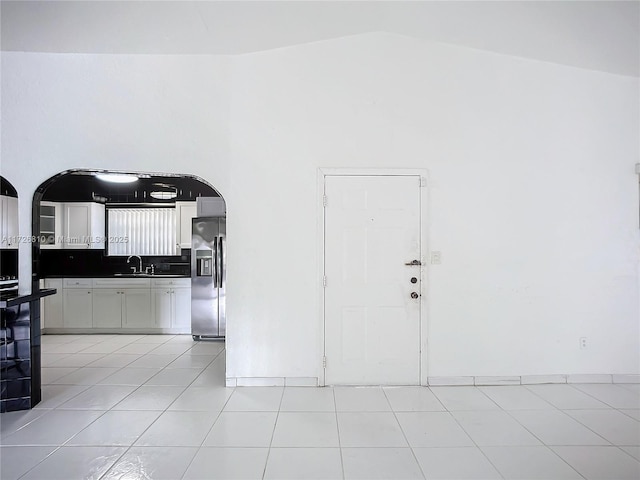 interior space featuring tasteful backsplash, vaulted ceiling, stainless steel refrigerator with ice dispenser, light tile patterned flooring, and white cabinets