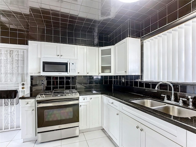 kitchen featuring white cabinets, dark stone countertops, sink, stainless steel range with gas cooktop, and light tile patterned floors