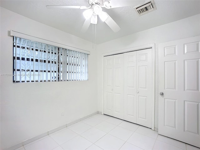 unfurnished bedroom with ceiling fan, light tile patterned floors, a closet, and a textured ceiling