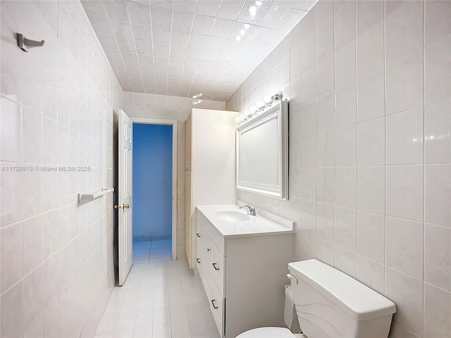 bathroom with tile walls, toilet, vanity, and tile patterned flooring