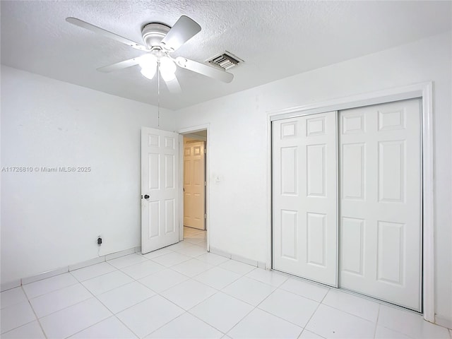 unfurnished bedroom with ceiling fan, a textured ceiling, light tile patterned floors, and a closet