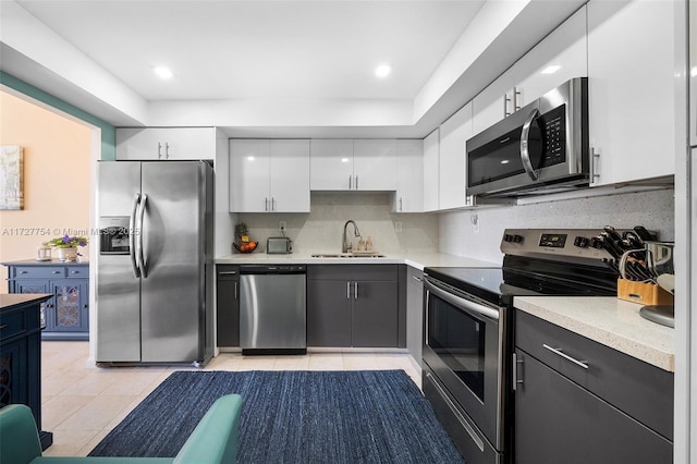 kitchen with light tile patterned flooring, sink, white cabinetry, appliances with stainless steel finishes, and decorative backsplash