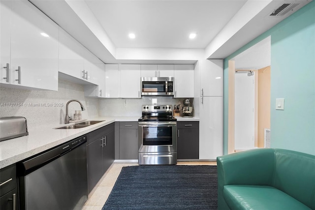 kitchen with light tile patterned flooring, appliances with stainless steel finishes, tasteful backsplash, sink, and white cabinets