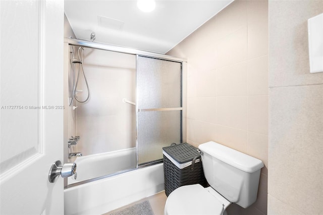 bathroom featuring tile walls, enclosed tub / shower combo, and toilet