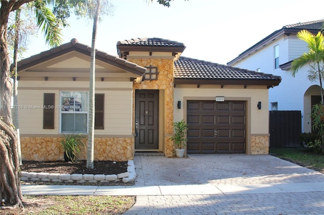 mediterranean / spanish-style house featuring decorative driveway, stone siding, a tiled roof, and an attached garage