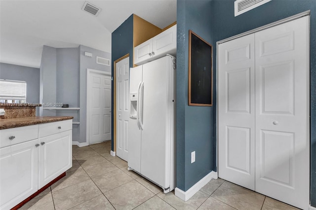 kitchen featuring light tile patterned floors, white refrigerator with ice dispenser, visible vents, white cabinets, and dark countertops
