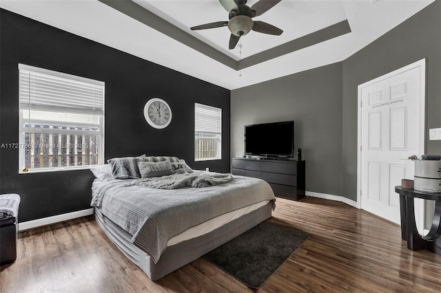 bedroom with a ceiling fan, baseboards, a raised ceiling, and wood finished floors