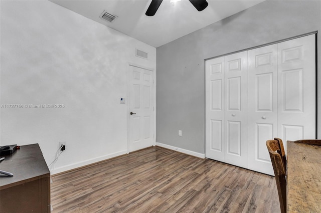 unfurnished office featuring a ceiling fan, visible vents, baseboards, and wood finished floors
